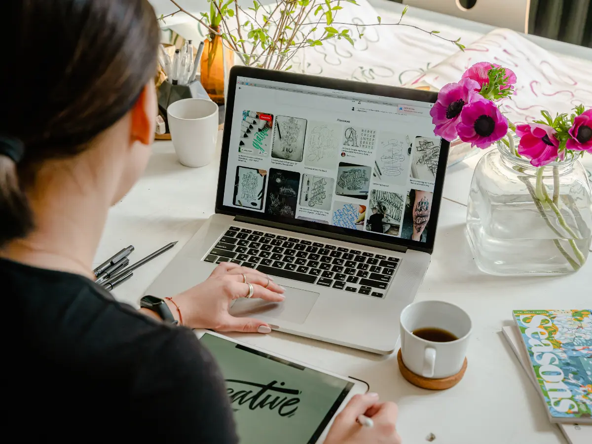 Person working on a laptop displaying creative designs, surrounded by coffee and flowers, illustrating digital marketing and web design inspiration.